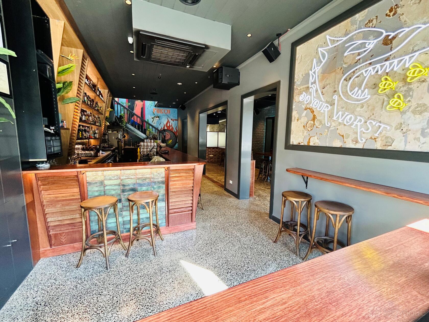 A bar with high wooden stools, wall art, and a backlit liquor display at Next D'Or Tapas Hawthorn.