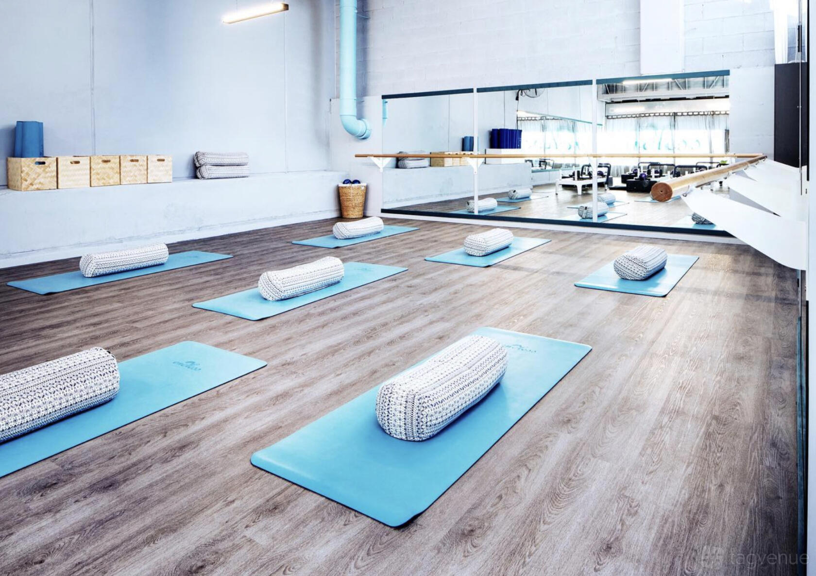 A yoga studio with blue mats, patterned bolsters, wood floors, and mirrored wall at Endless Lifestyle Studio.