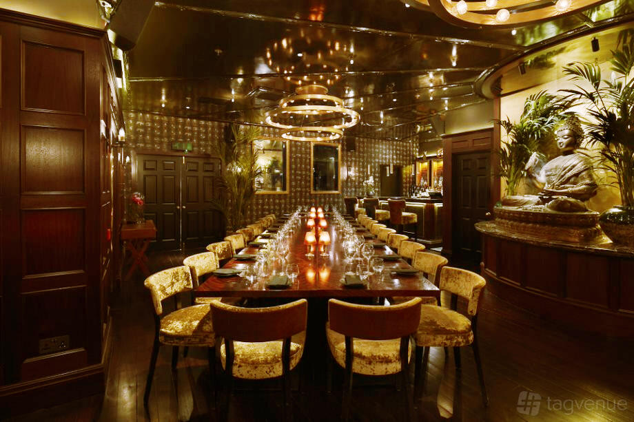 An event space in a restaurant with a long banquet table, golden chairs, decorative lighting, and a Buddha statue at TATTU.