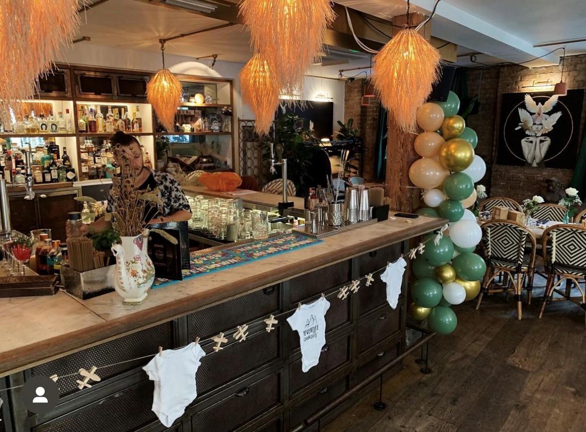 An event space in a restaurant with a decorated bar, pendant lights, and a colorful balloon arrangement at The Last Talisman.