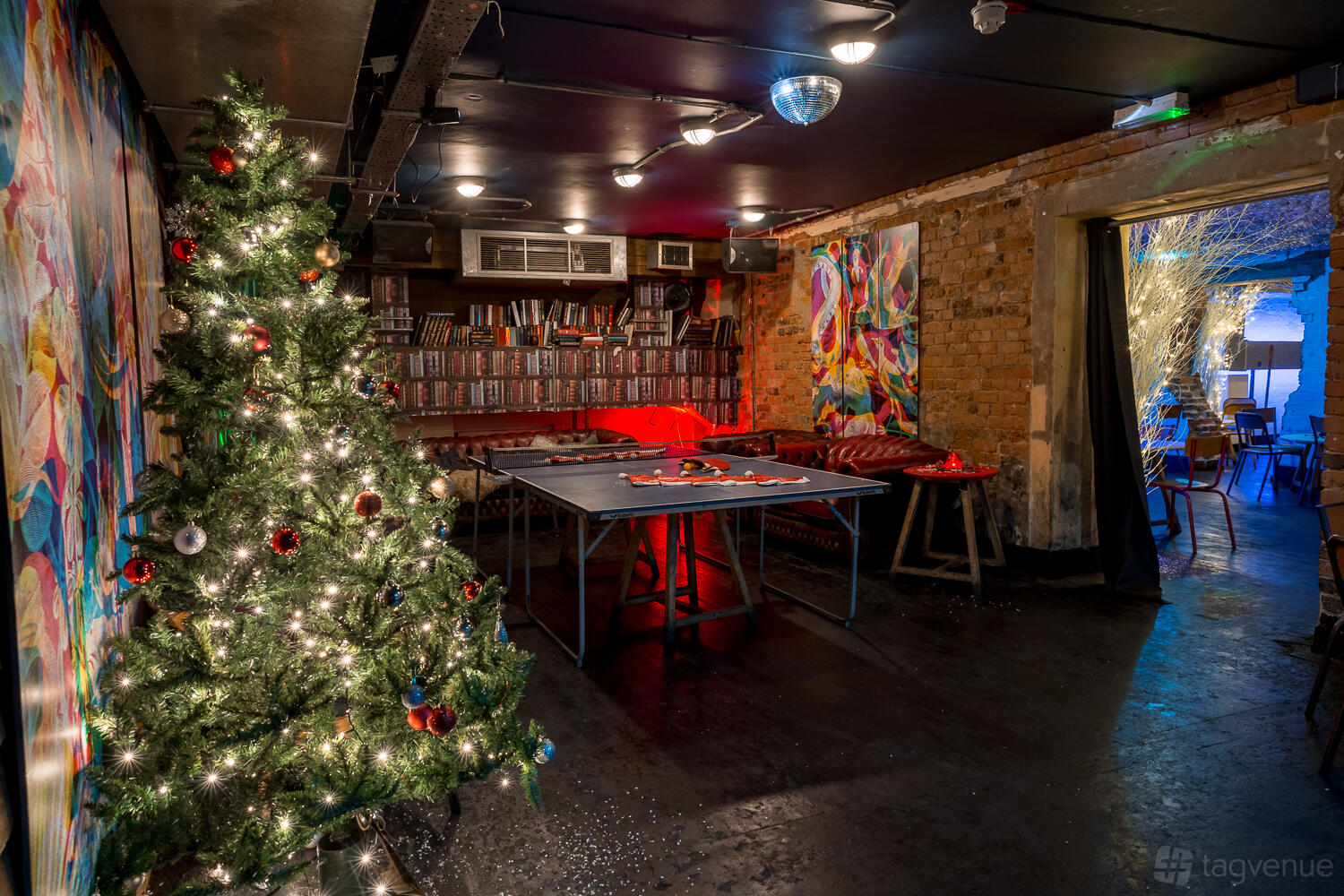 A nightclub in a bar with exposed brick walls, a lit Christmas tree, and a ping pong table at The Book Club.