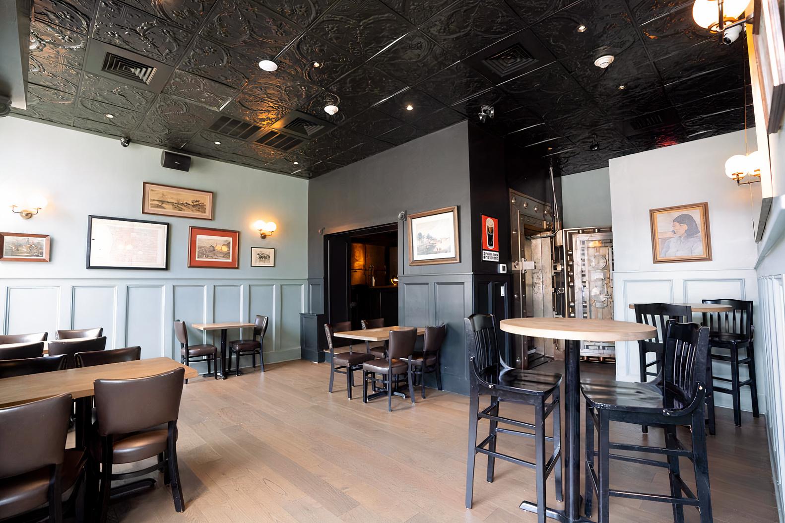 A bar with dark wood tables, vintage framed art, and a decorative patterned ceiling at The Mulberry.