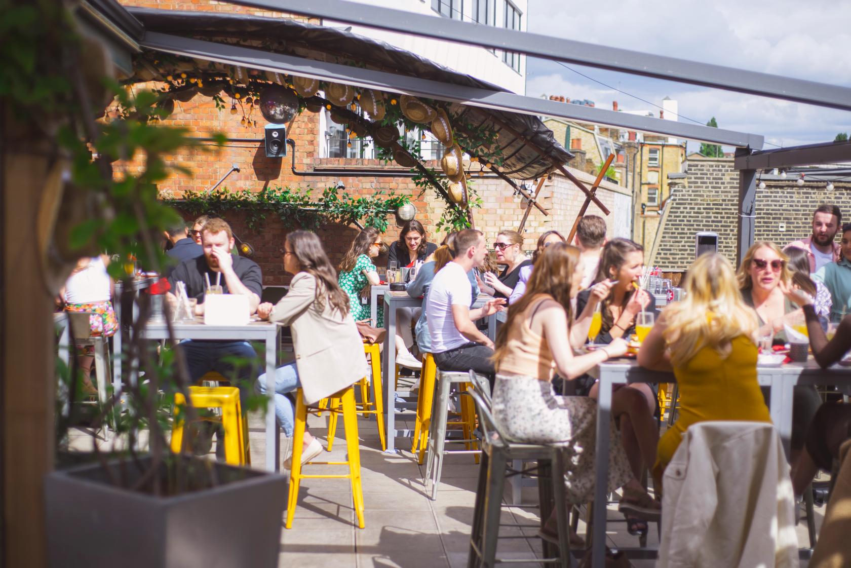 An outdoor bar area with high tables, yellow stools, and a pergola at Big Chill Kings Cross.