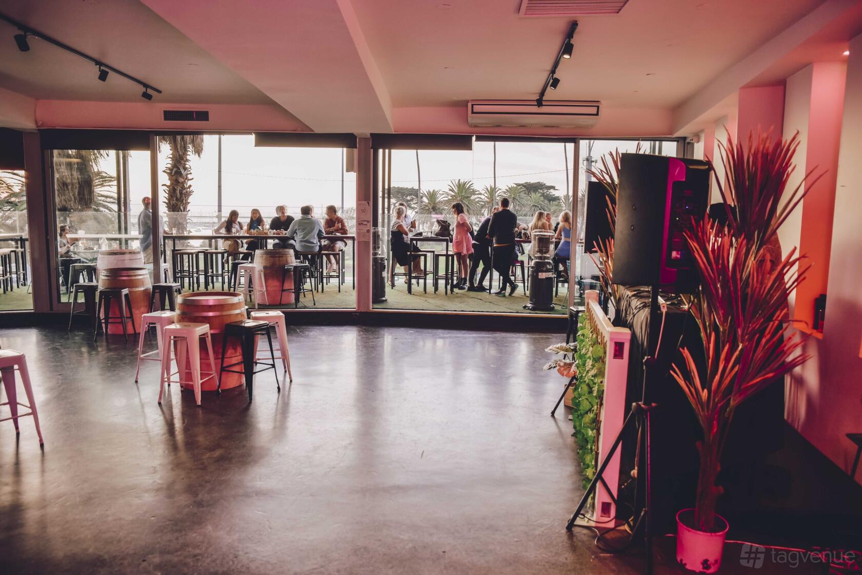 A rooftop cocktail bar with polished floors, potted plants, and glass doors opening to an outdoor seating area at Ellora.
