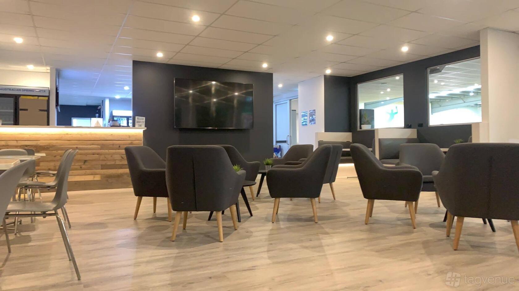 An event space with dark armchairs, light wood flooring, and a large wall-mounted TV at Gravity Zone.