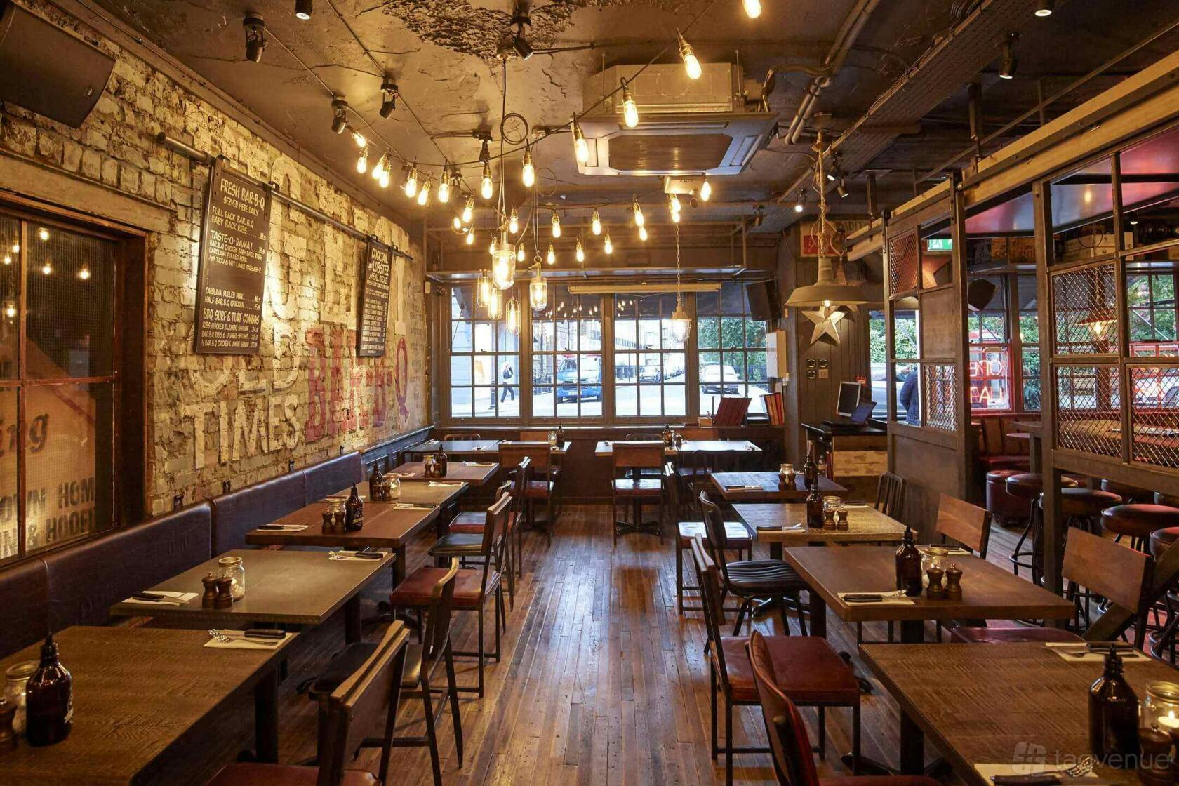 A restaurant with exposed brick walls, hanging Edison bulbs, and wooden tables at Big Easy Restaurant - Kings Road, Chelsea.