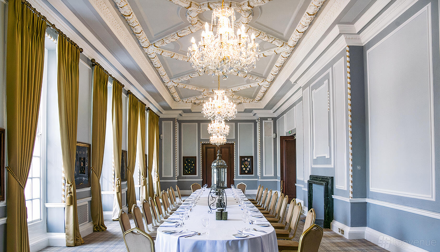 An event space with ornate chandeliers, tall windows with gold curtains, and a long banquet table at Manchester Hall.