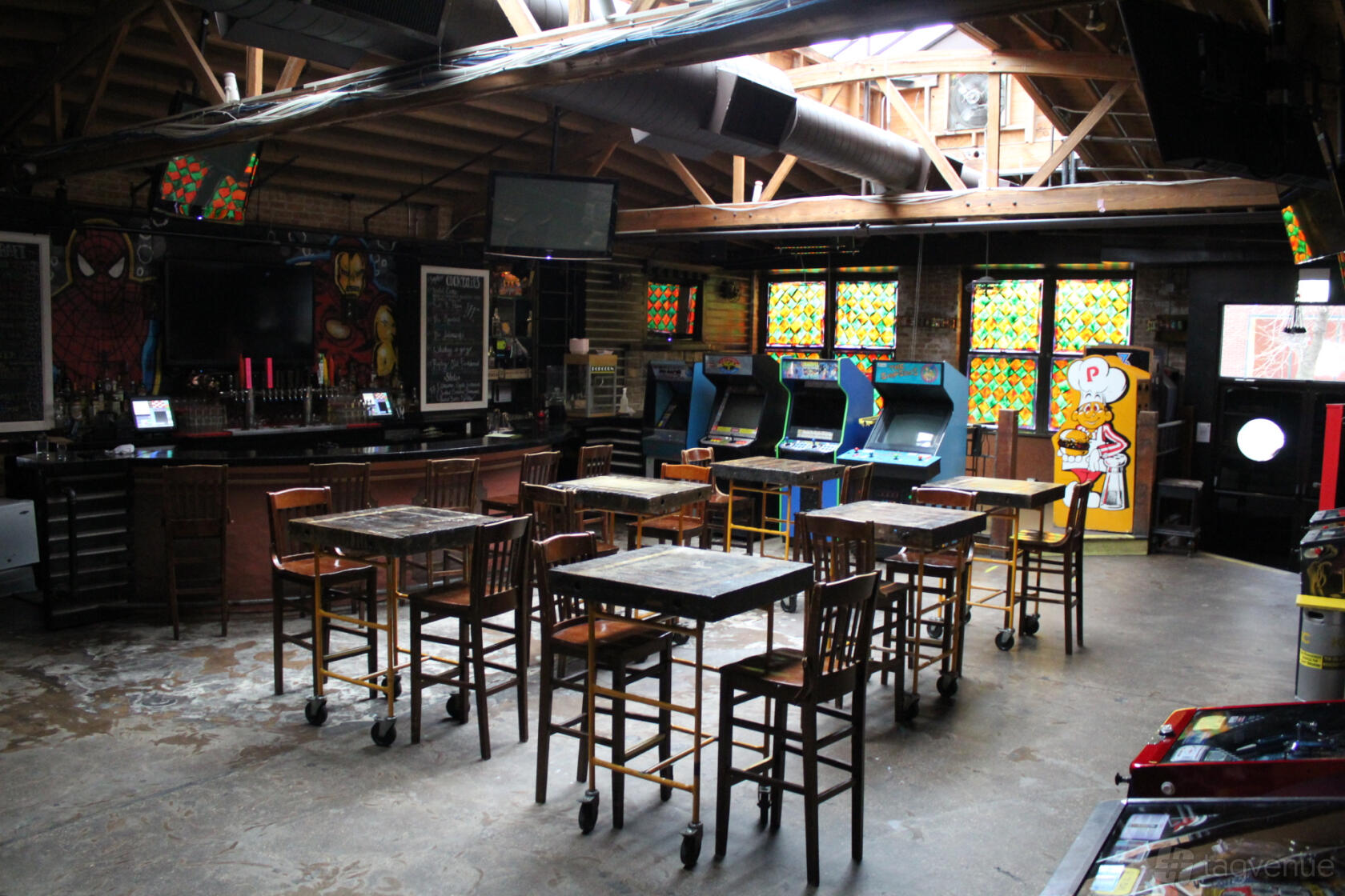 A bar with high-top tables, wooden beams, arcade machines, and stained glass windows at Replay Lincoln Park.