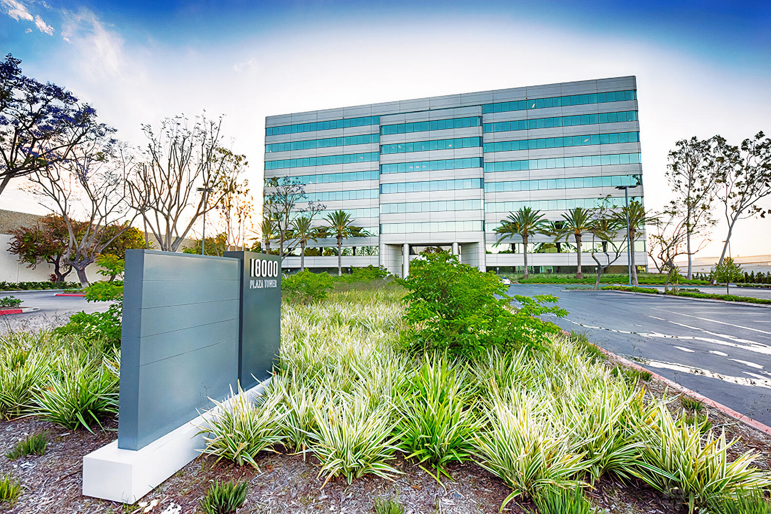 An office building with glass windows, landscaped entrance beds, and palm trees at Premier Workspaces - Cerritos.
