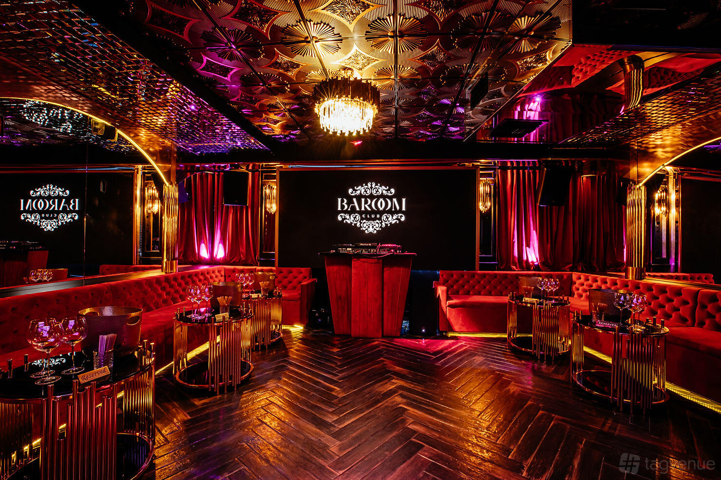 An event venue with tufted red velvet seating, mirrored ceiling, and a central chandelier at Baroom Club.