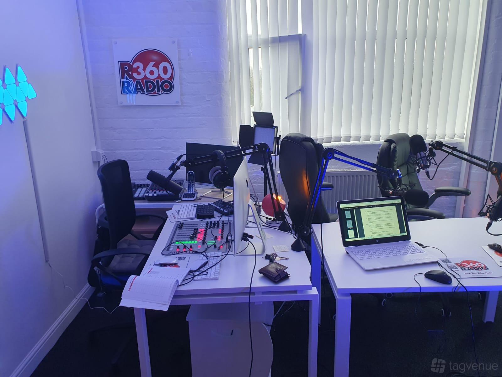 A recording studio with microphones, headphones, and computer screens on white desks at R360 Studio.