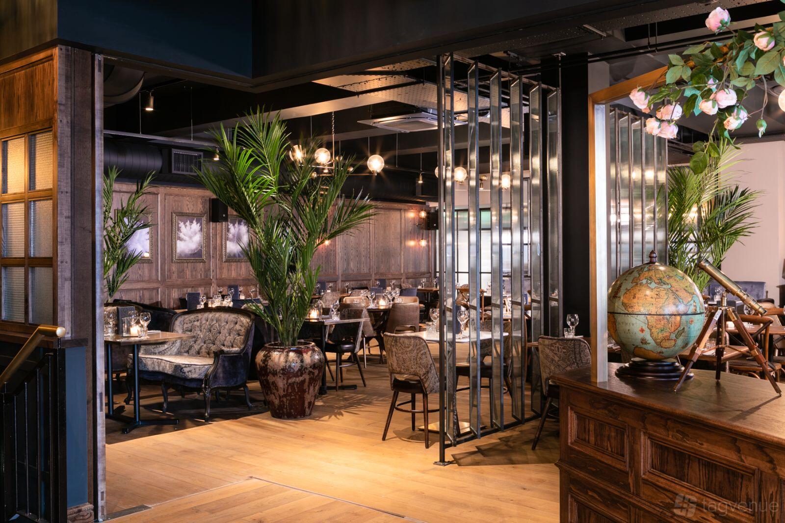 A dining room with wood flooring, leafy plants, globe decor, and tables set with glassware at The Lost & Found Bristol.
