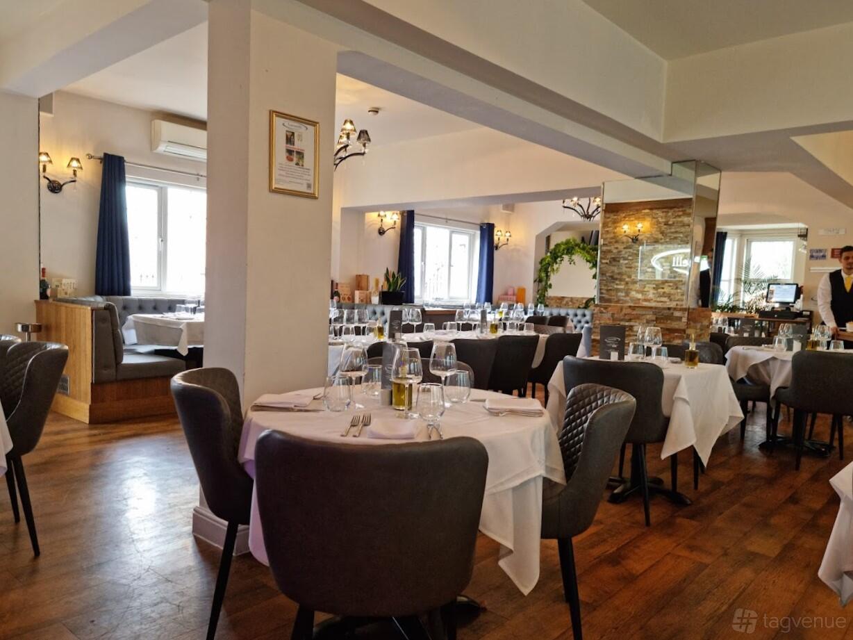 A dining room with round tables set with white linens, padded chairs, and wood floors at Lucarelli West Bromwich.