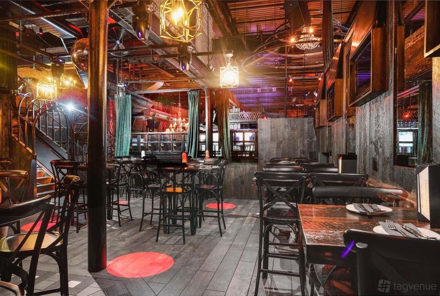 A bar with high tables, dark wood flooring, and exposed ceiling pipes on the third floor at The Ashford.
