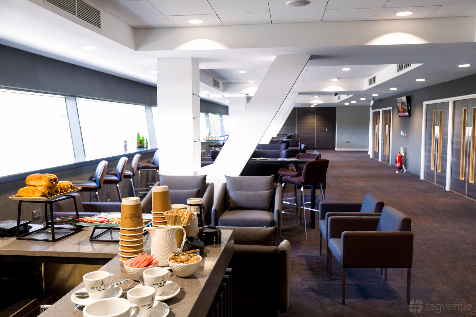 A stadium lounge with floor-to-ceiling windows, armchairs, and a coffee service station at Ashton Gate Stadium.