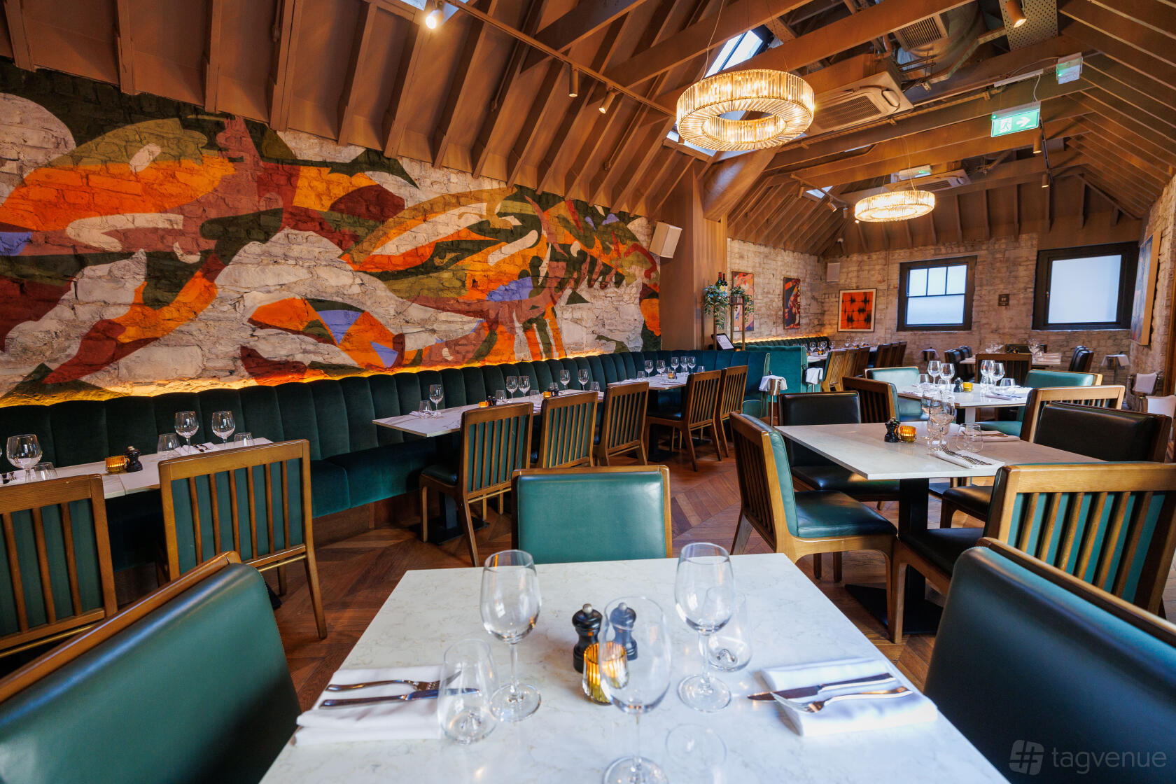 An event space with exposed brick walls, colorful mural, and set dining tables at Lennan's Yard.