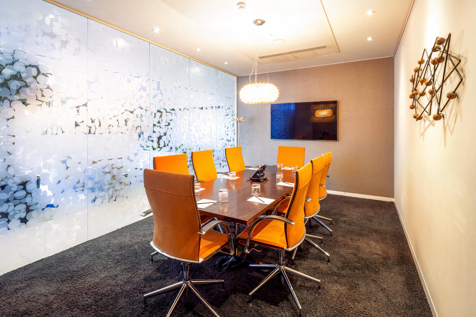 A meeting room with a long table, orange leather chairs, frosted glass wall, and pendant lighting at Landmark: Heron Tower, London.