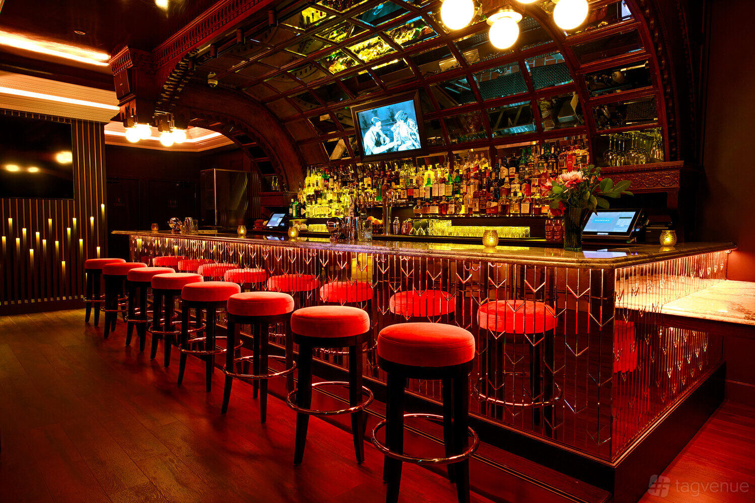 A cocktail bar with red velvet stools, an art deco mirrored bar, and warm ambient lighting at DecoDance Bar.