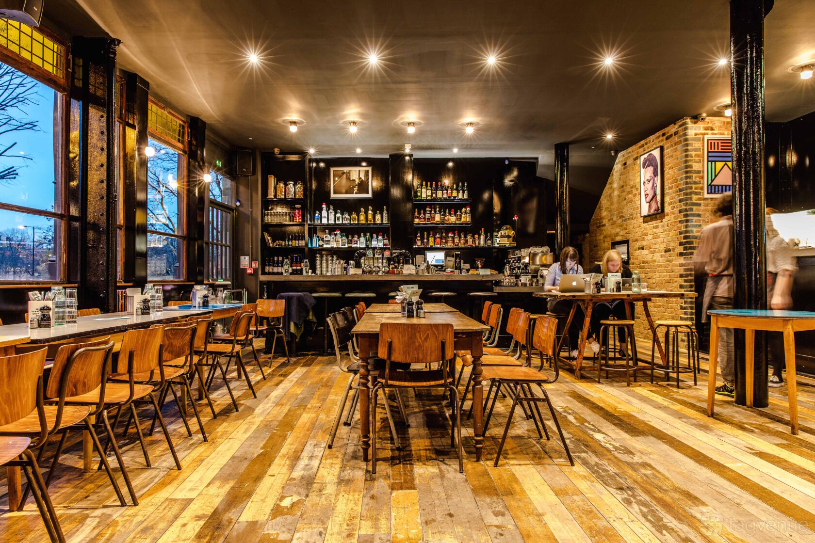 An event space in a bar with wooden floors, exposed brick walls, large windows, and a well-stocked central bar at Coin Laundry.