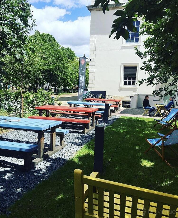 An outdoor area with colorful picnic tables and deck chairs beside the Dreadnought Building.