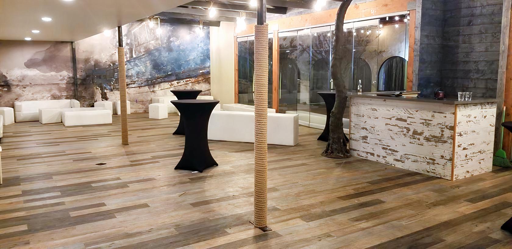 An event venue with rustic wooden floors, cocktail tables draped in black linens, and a white lounge area at Encore Event Center.