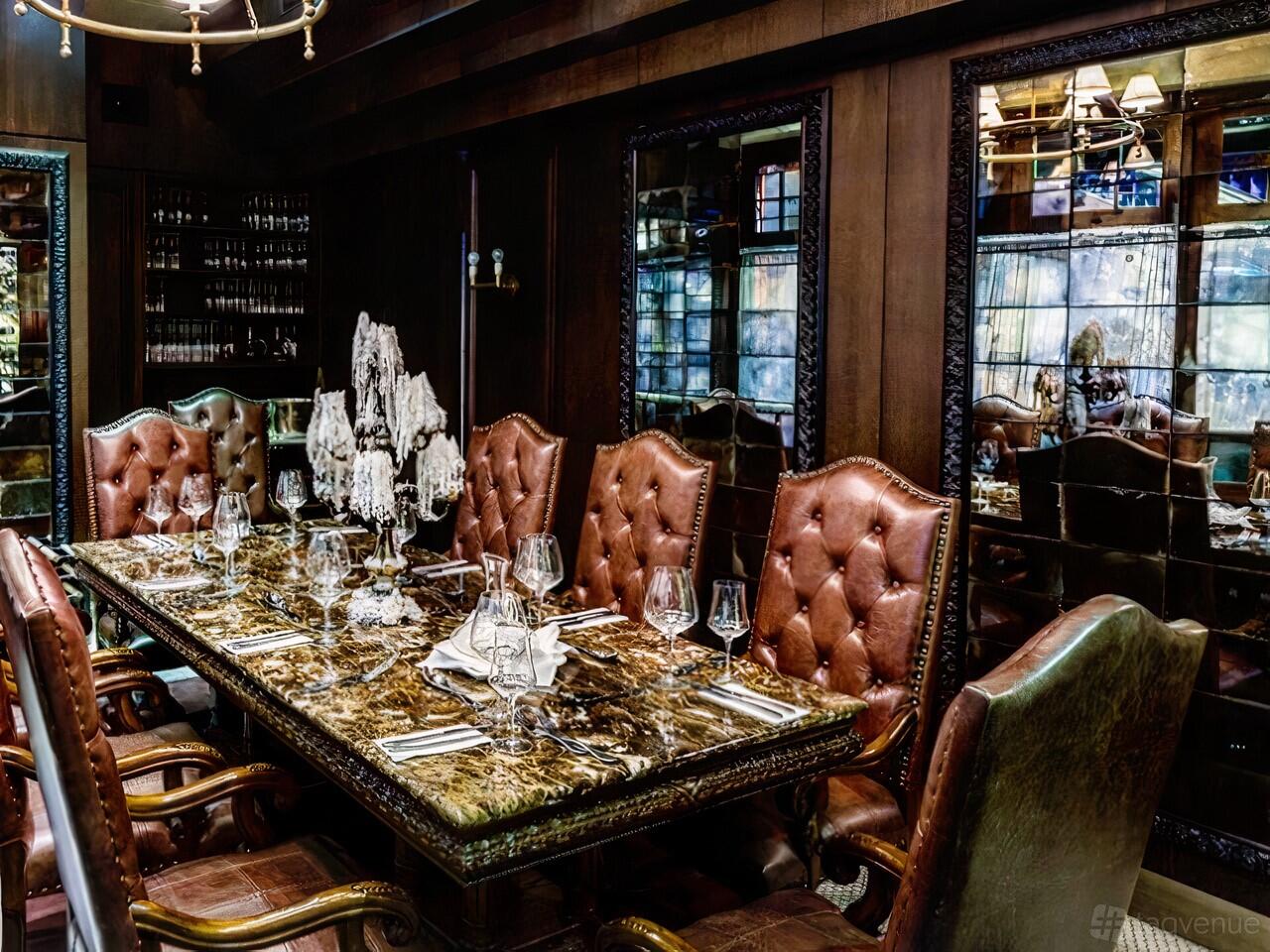 A dining room with a long marble table, tufted leather chairs, and mirrored walls at Baia The Italian.