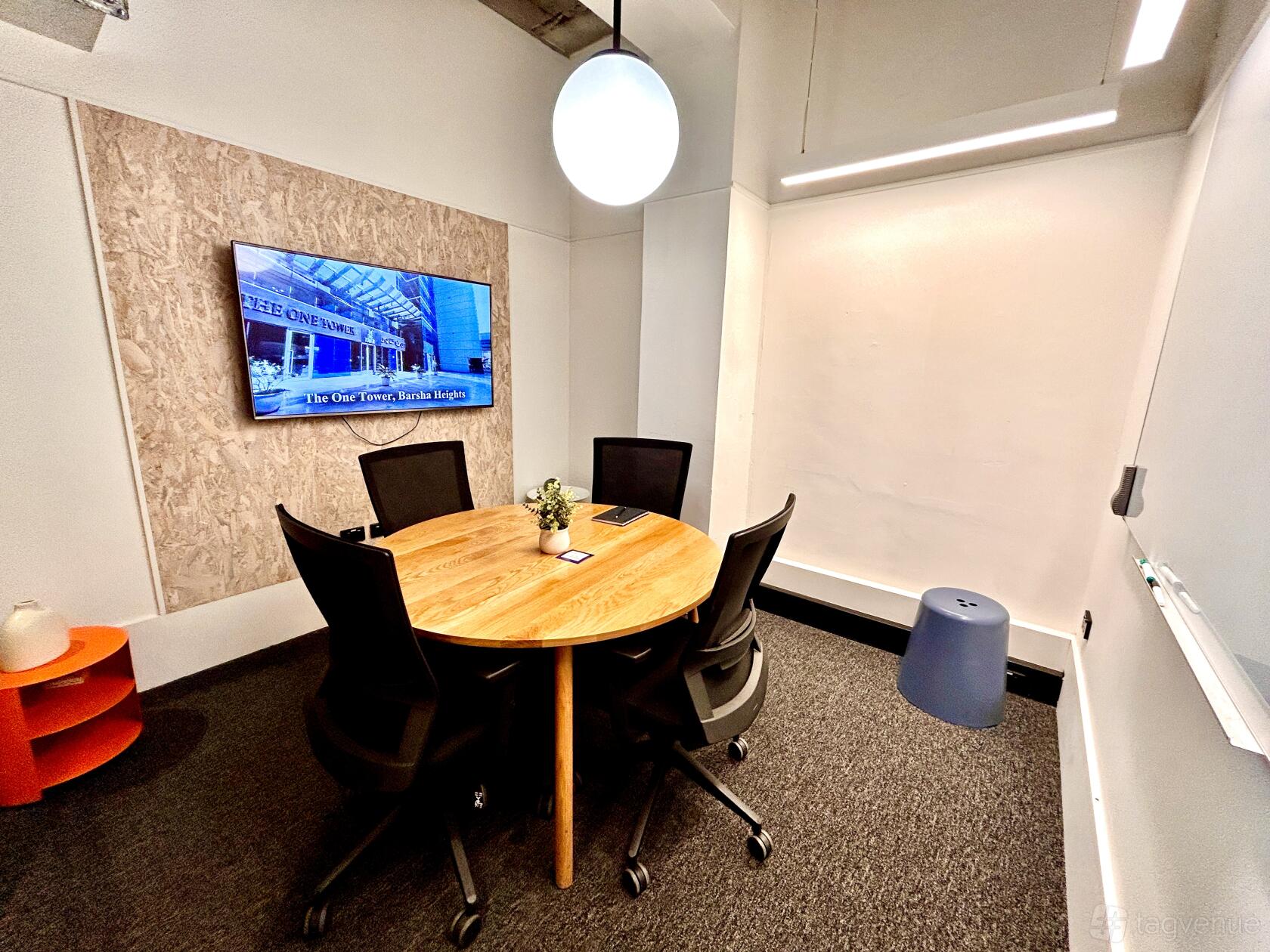 A meeting room with a round wooden table, four black chairs, a wall-mounted screen, and a whiteboard at Czar Workspace.