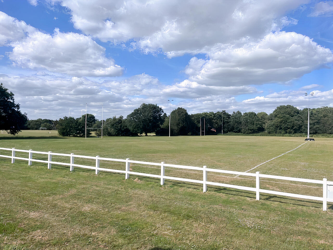 An open rugby and football field with white boundary fencing and goalposts at Old Cranleighan Sports Club.
