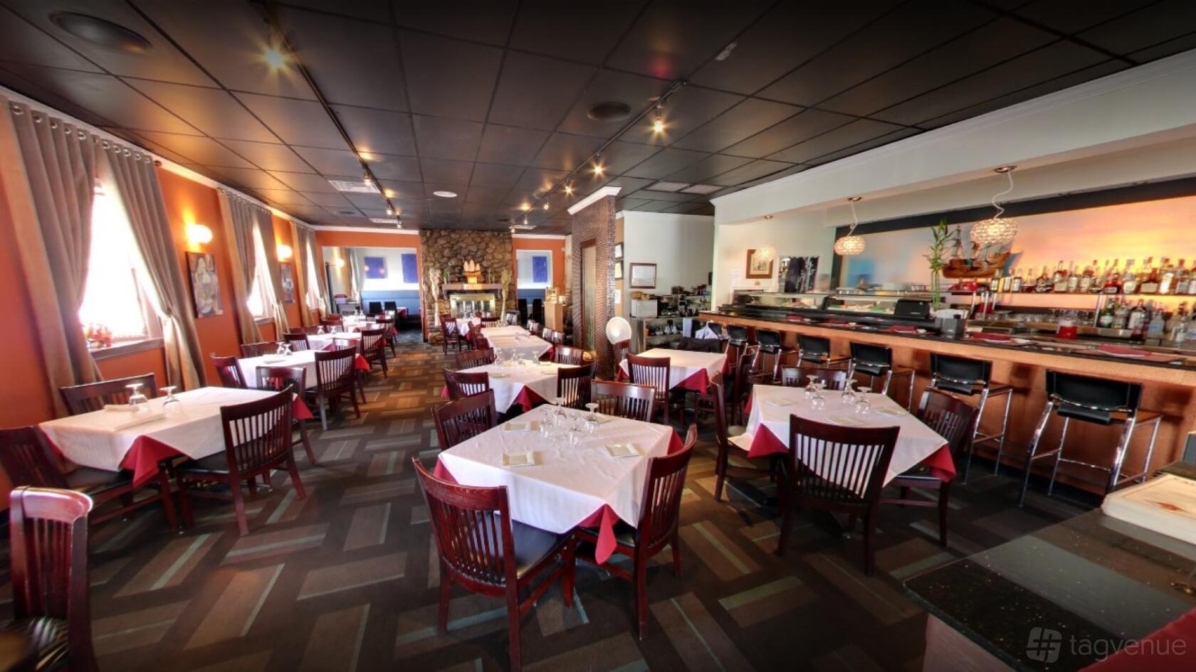 A restaurant with white tablecloths, wooden chairs, and a stone fireplace at Rain Thai & Sushi Bar.