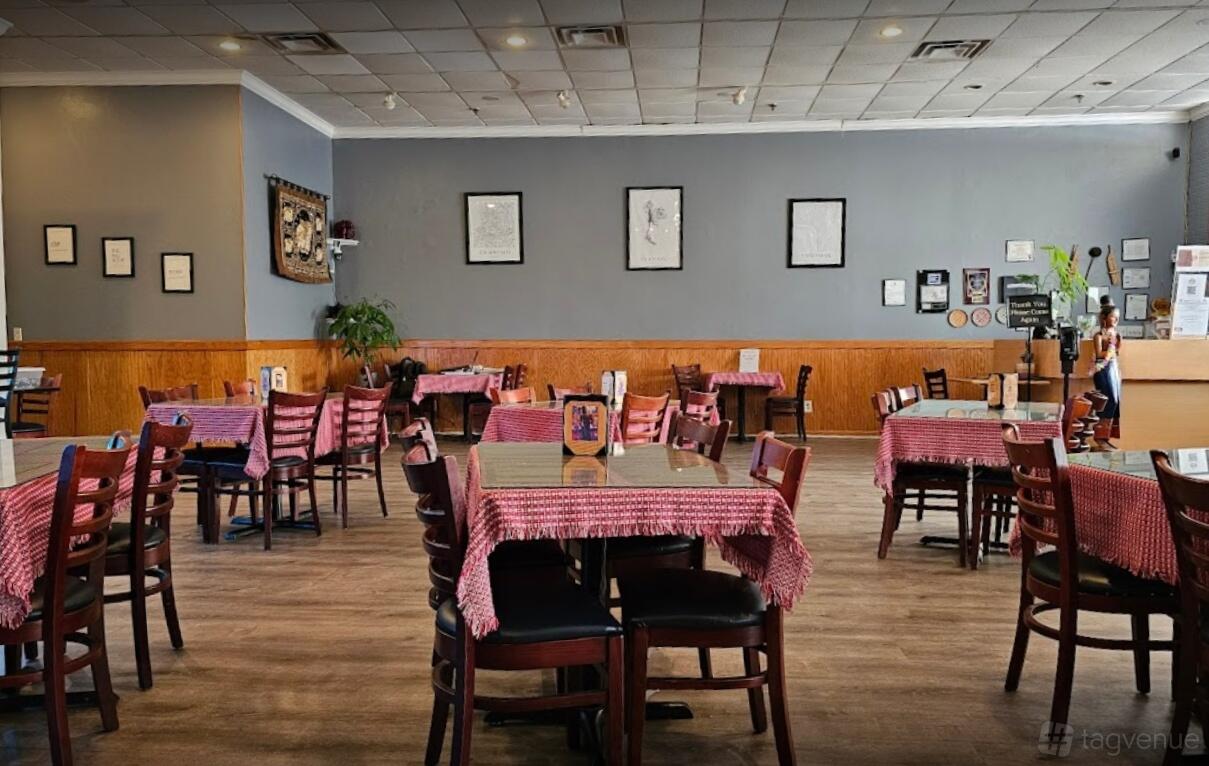 A restaurant with tables covered in red patterned cloths, wooden chairs, and framed art at Saap Lao Thai Cuisine & Bar.