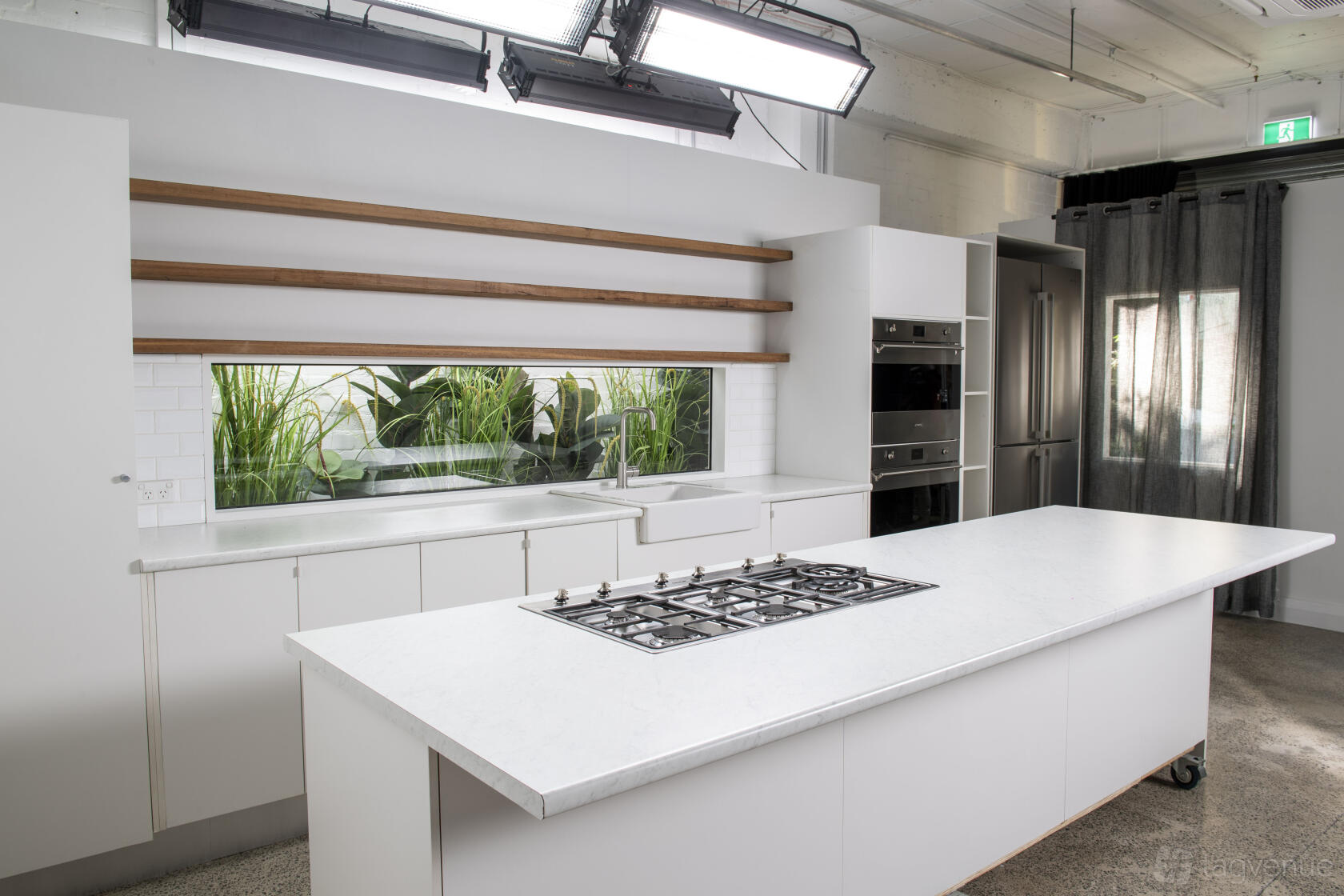 A kitchen in a photo studio with a white island cooktop, open wood shelves, and a window with greenery at Cutaway Studio.