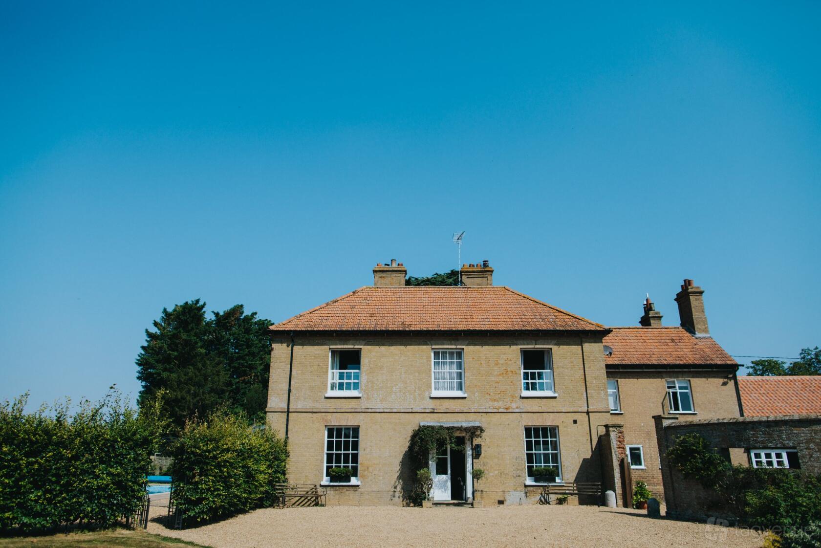 A country house with a red-tiled roof, tall chimneys, and gravel driveway at Godwick Hall.