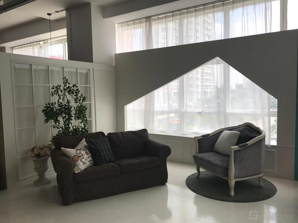 A photo studio with large geometric windows, sheer curtains, and cozy seating at Shine & I Baby Photo Studio.
