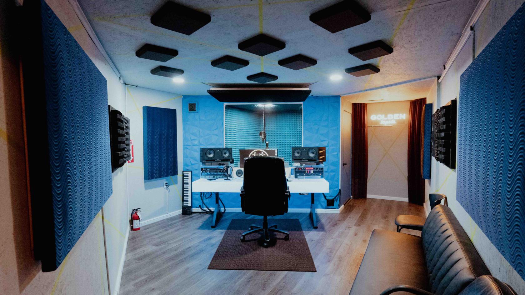 A recording studio with soundproofed walls, a mixing desk, studio monitors, and acoustic panels at Golden Impala Recording Studio.