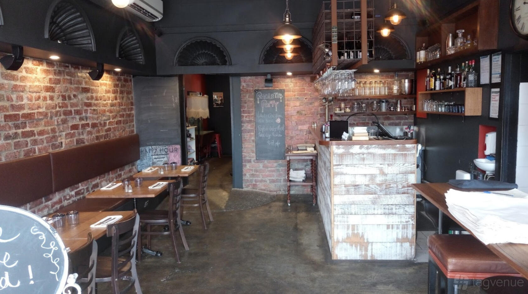 An event space in a restaurant with exposed brick walls, wooden tables, and a rustic bar at The Little French Deli & Bistro.