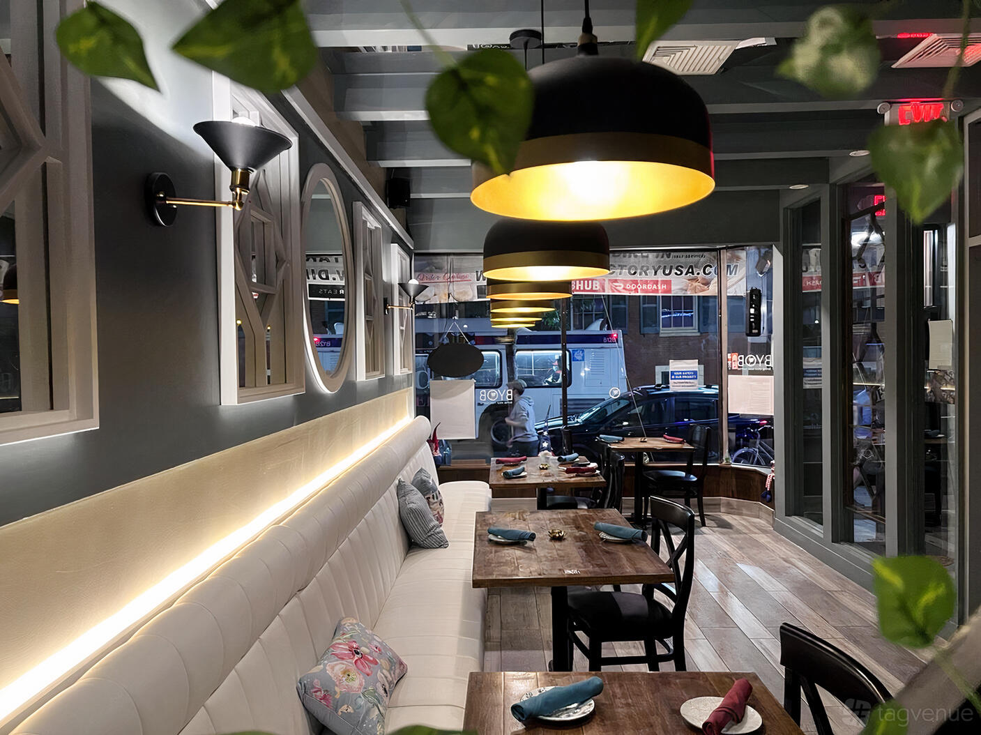 A restaurant with wooden tables, black chairs, pendant lighting, and large front windows at Grandma's Philly.
