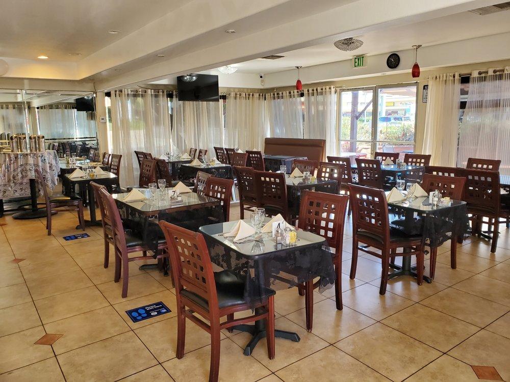 A restaurant dining room with dark wood chairs, tables set with white napkins, and large windows at New India Palace.