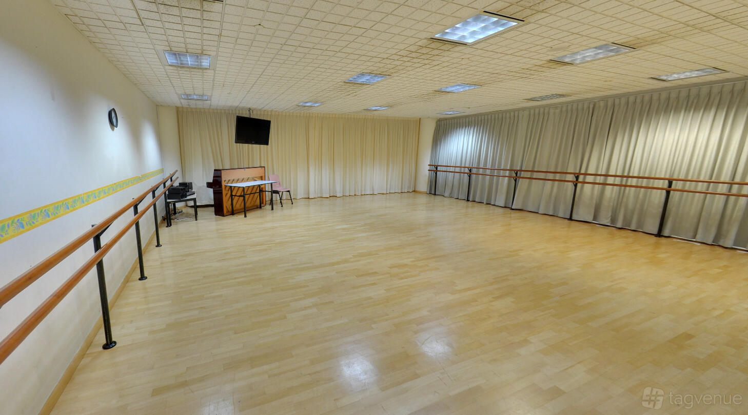 A dance studio with wooden floors, wall-mounted mirrors, ballet barres, and a piano at Crestar School of Dance @ Woodland Center.