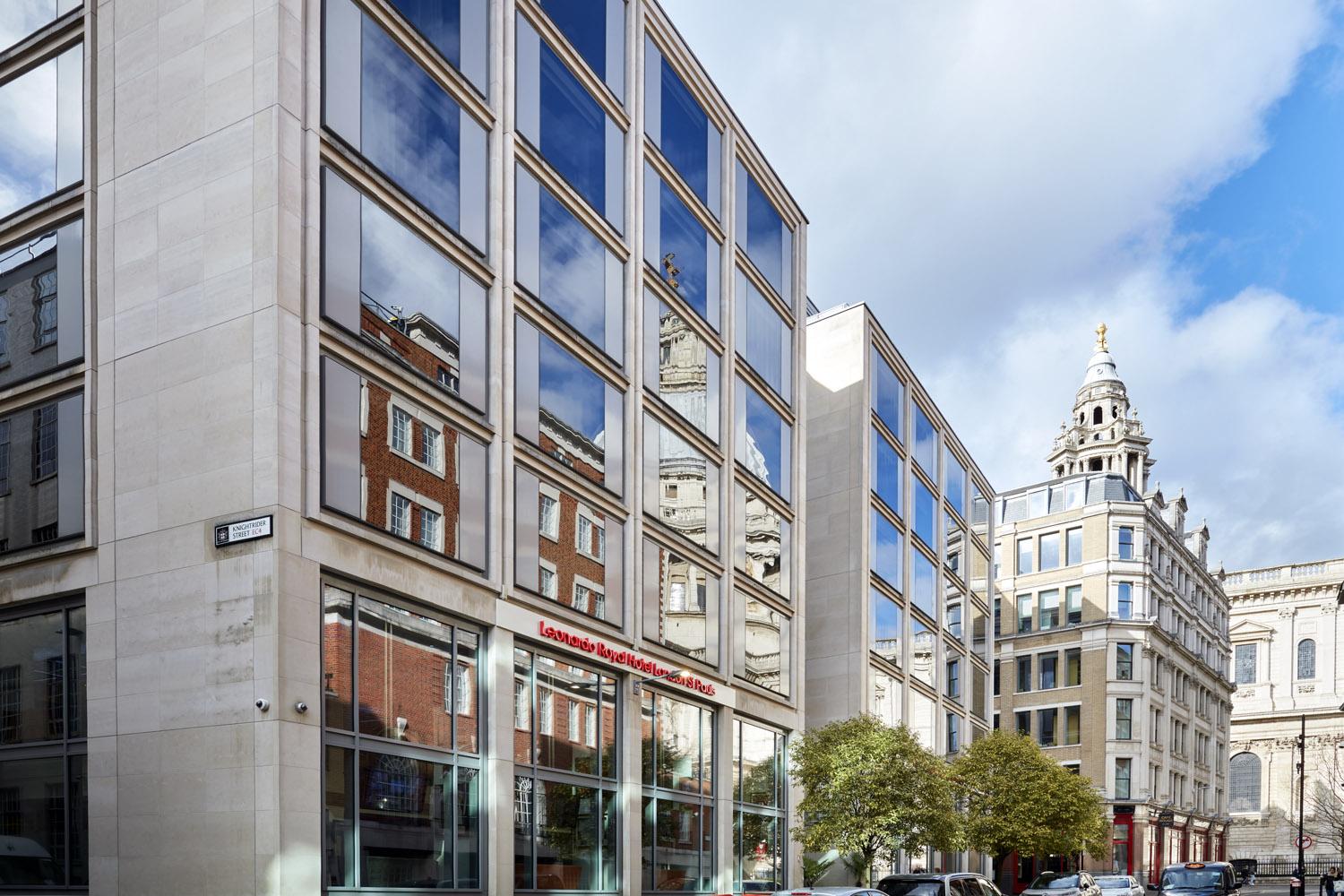 A hotel with a glass facade reflecting historic buildings and a street entrance at Leonardo Royal London St Paul's.