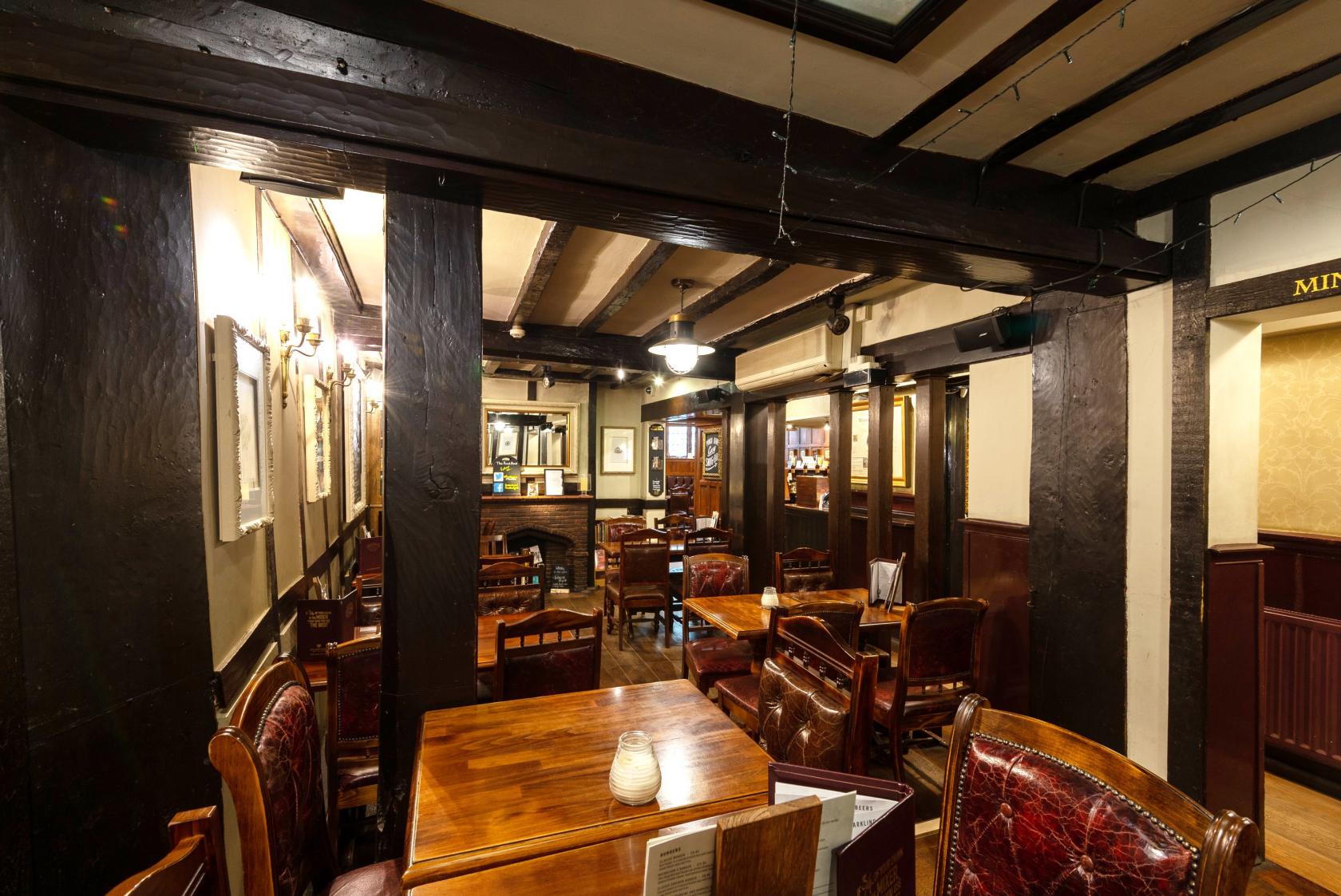A pub dining room with dark wood beams, framed pictures on cream walls, and leather armchairs at The Pump House.