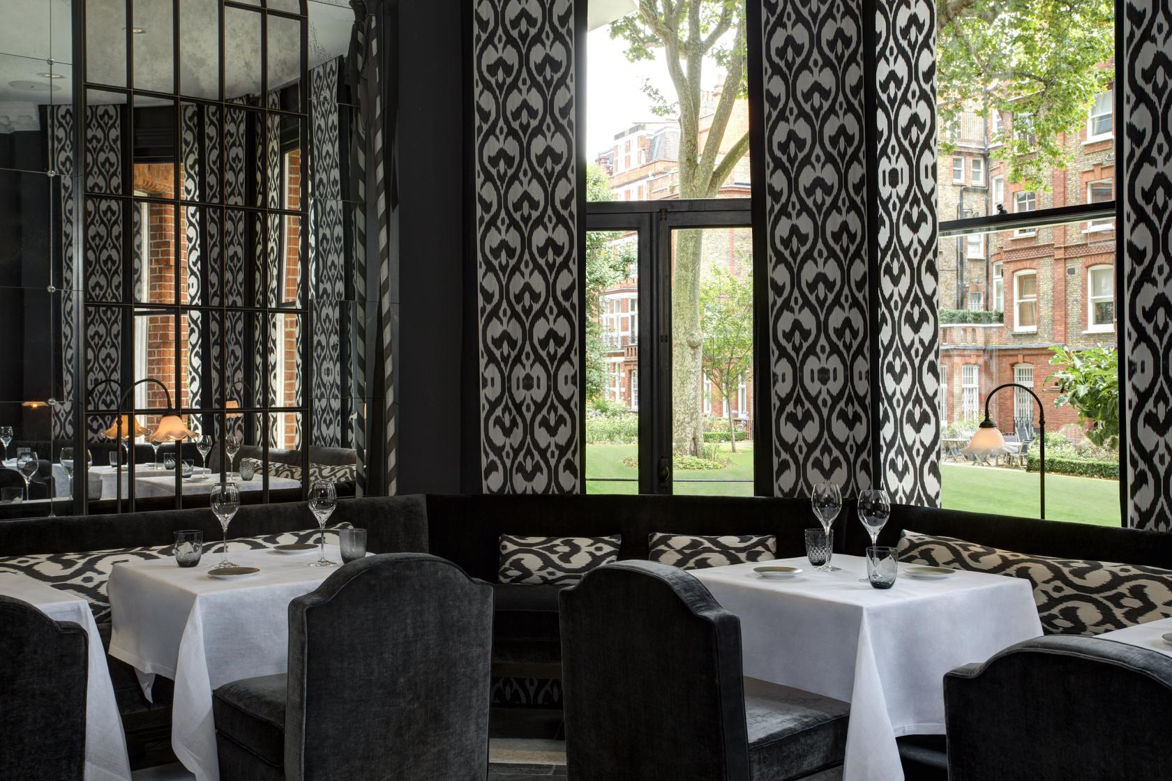 A hotel restaurant with patterned floor-to-ceiling drapes, mirrored walls, and white tablecloths at The Franklin London.