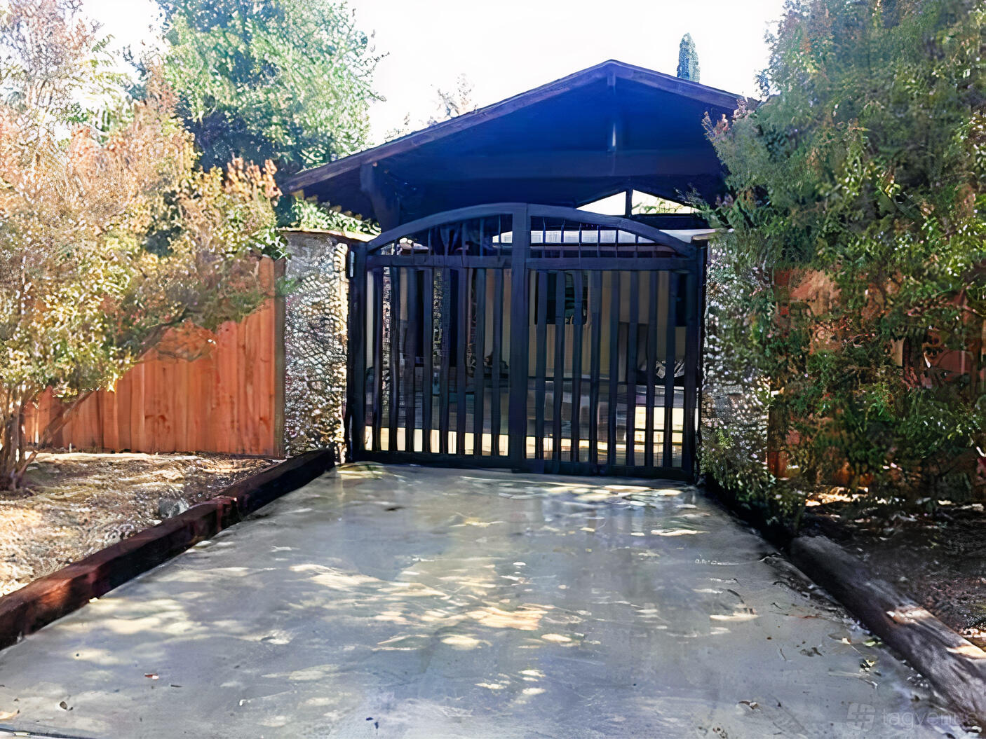 A gated entrance with a black iron gate, stone pillars, and surrounding trees at FWD Vision Spaces Thrive.