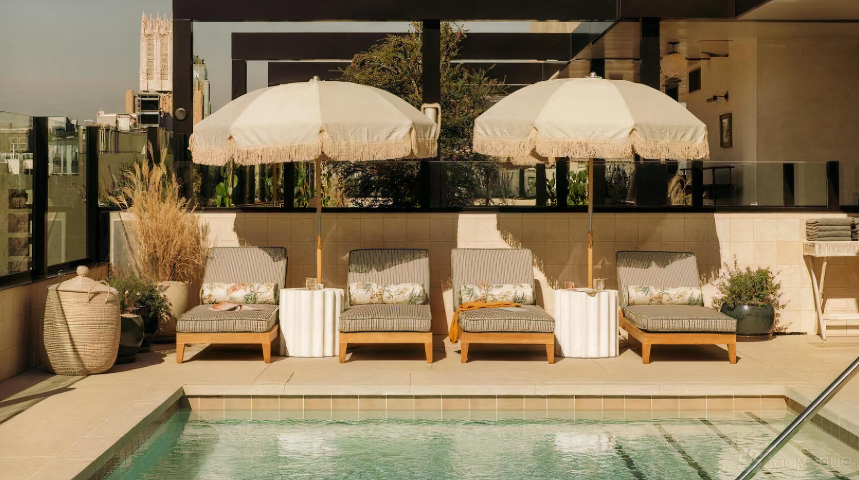 An outdoor restaurant pool deck with striped cushioned loungers, fringed umbrellas, and a clear swimming pool at Cabra Los Angeles.