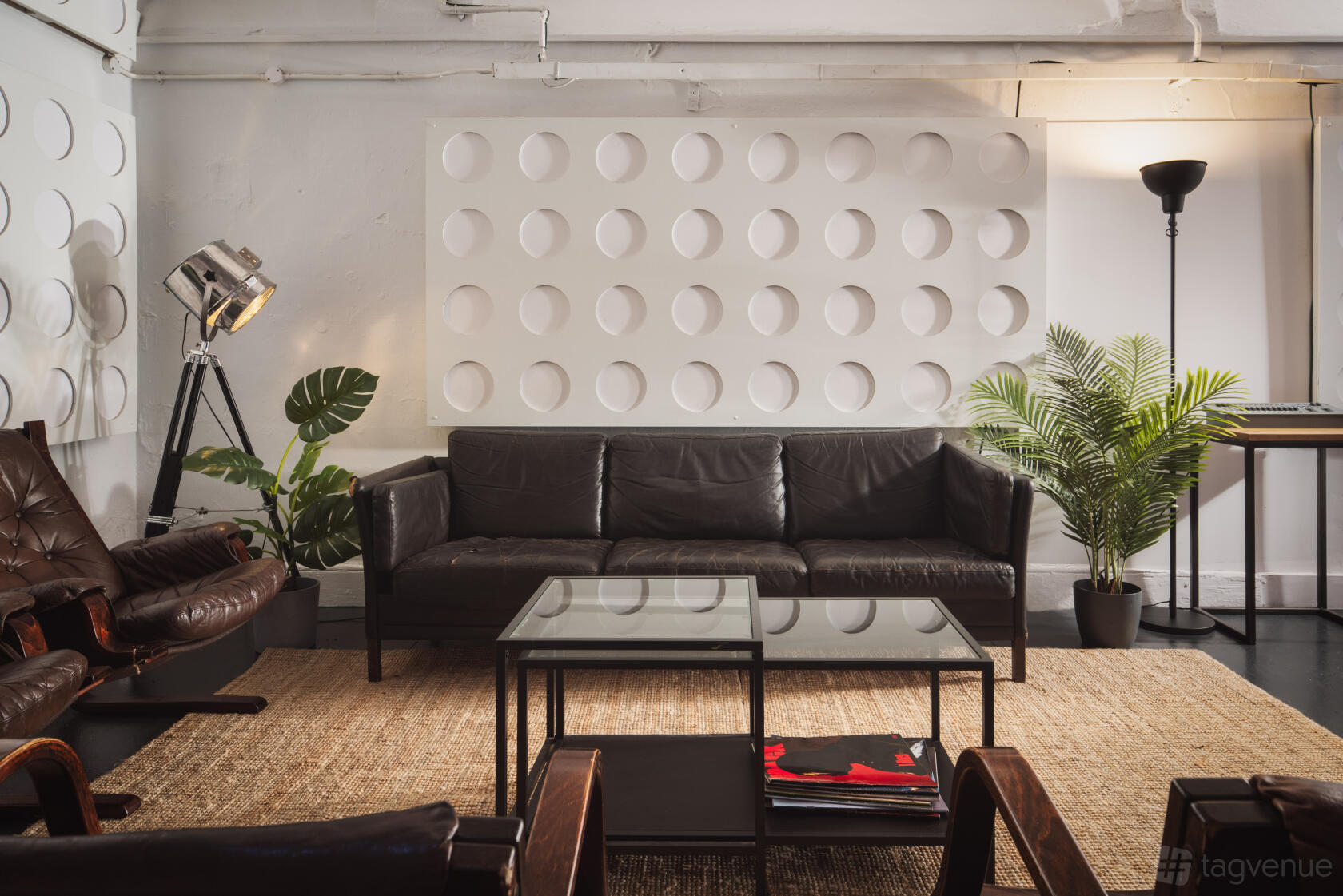 A rehearsal studio with black leather seating, glass coffee tables, potted plants, and textured wall panels at Factory Studios.