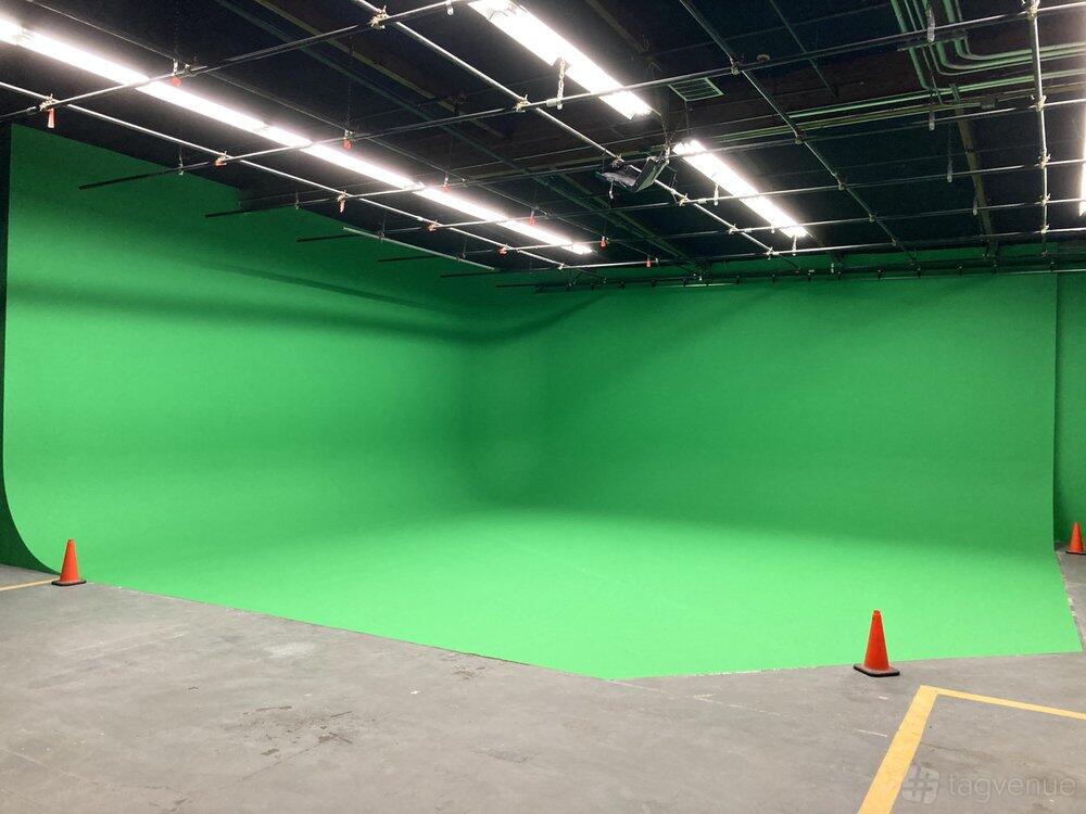 A photo studio with a large green cyclorama wall, grid ceiling lights, and orange safety cones at Minassian Productions, Inc.
