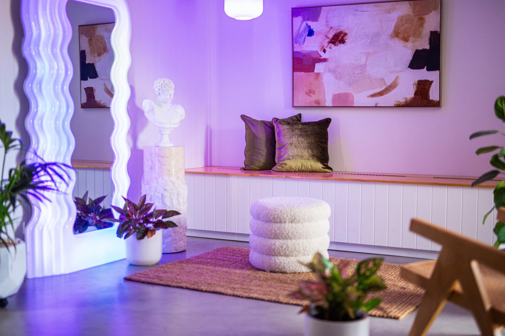 A photo studio with a large wavy mirror, abstract art, textured stools, and potted plants at Brewers St. Studio.