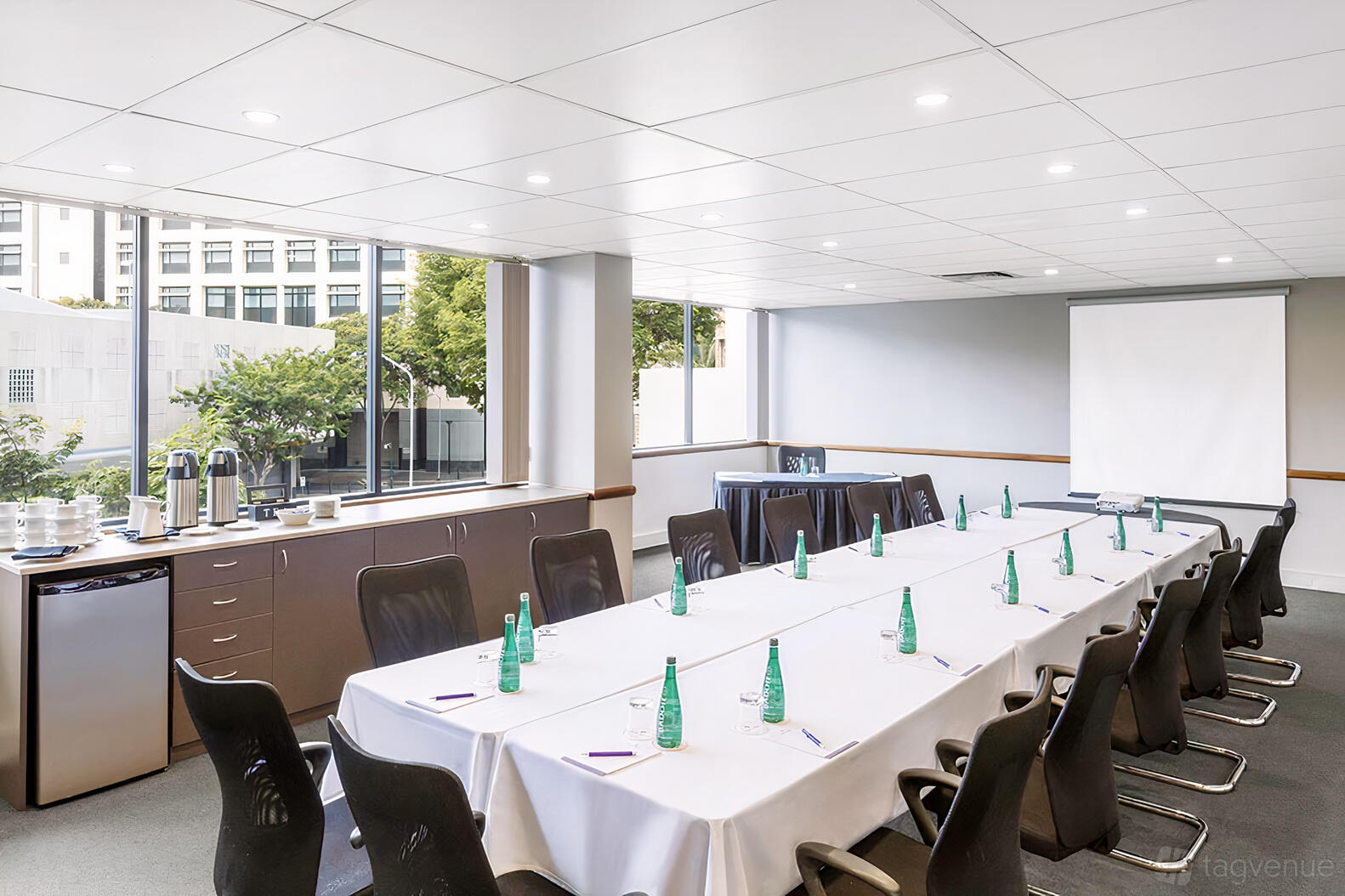 A meeting room with natural light, U-shaped table setup, conference chairs, and a projector screen at Park Regis North Quay.