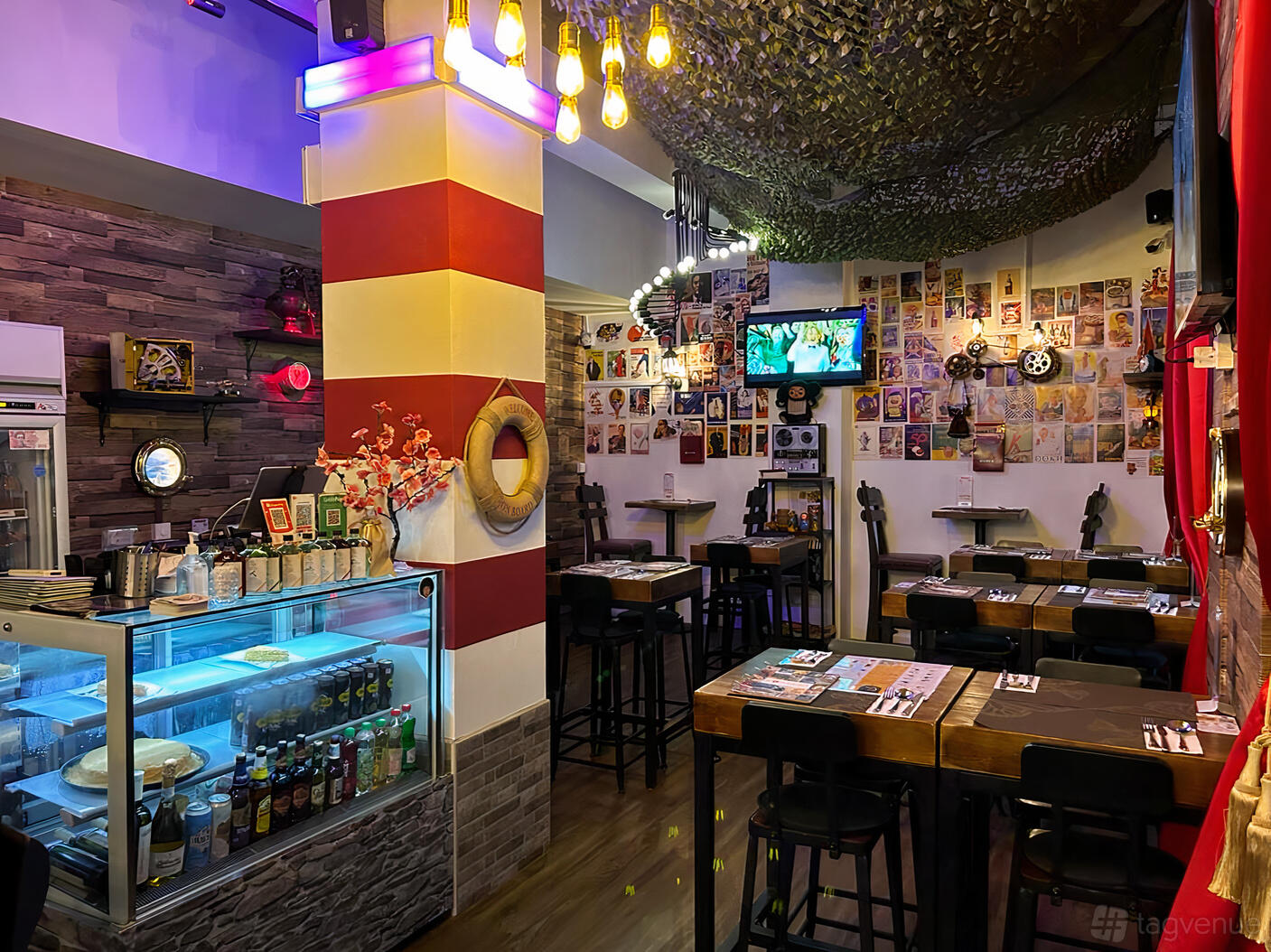 A restaurant with wall art, nautical decor, high tables, and a bar counter at Kapitan Bar and Bistro.
