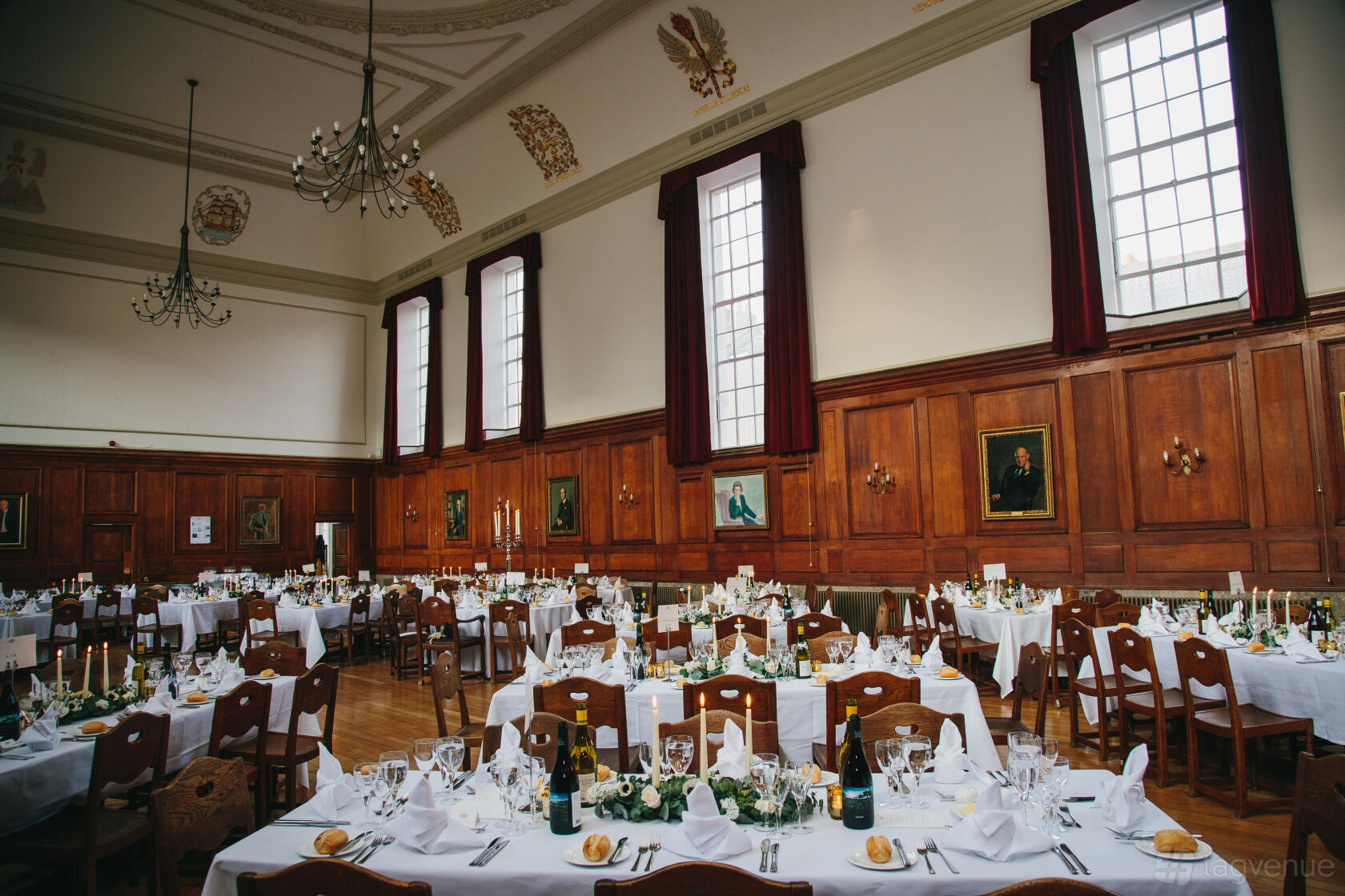 A grand hall with high ceilings, tall windows, wood-paneled walls, and banquet tables set for dining at Goodenough House.
