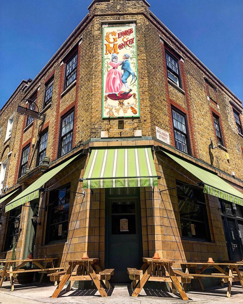 A pub with striped green awnings and exposed brick exterior at The George & Monkey.